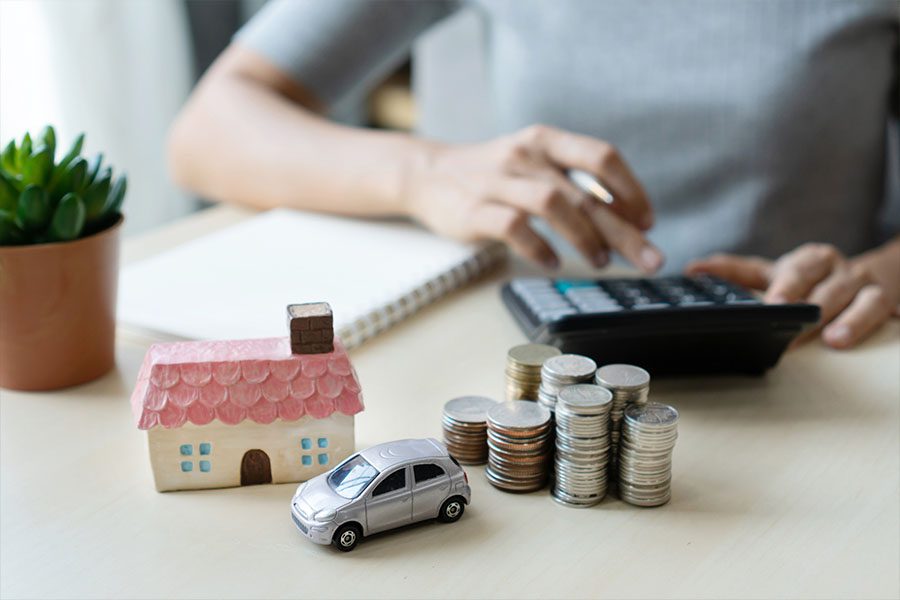 Bundling Home and Auto Insurance - Picture of a Womans Hands with a House and Car on the Desk